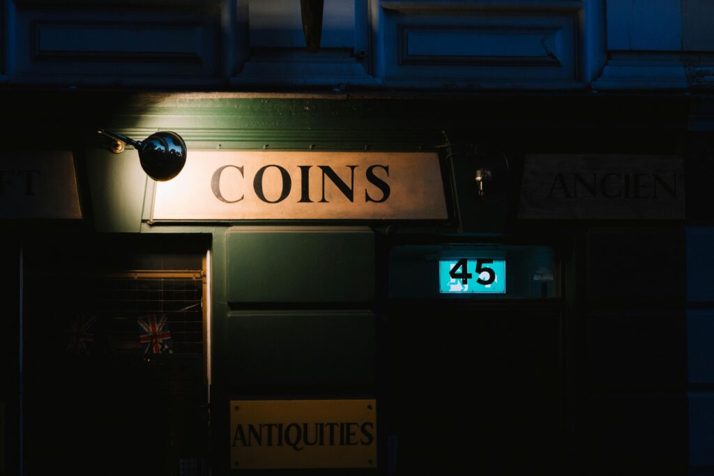 A vintage coin shop illuminated at night, showcasing signs and a streetlight.